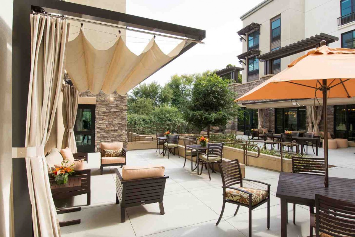A modern outdoor patio with comfortable seating and large umbrellas, surrounded by lush greenery.