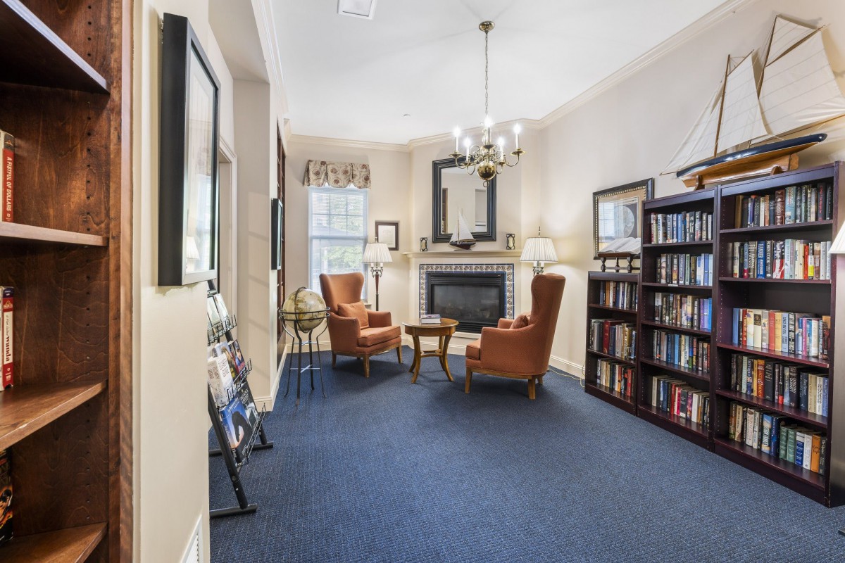 A cozy living room with armchairs, a fireplace, and a large bookshelf.