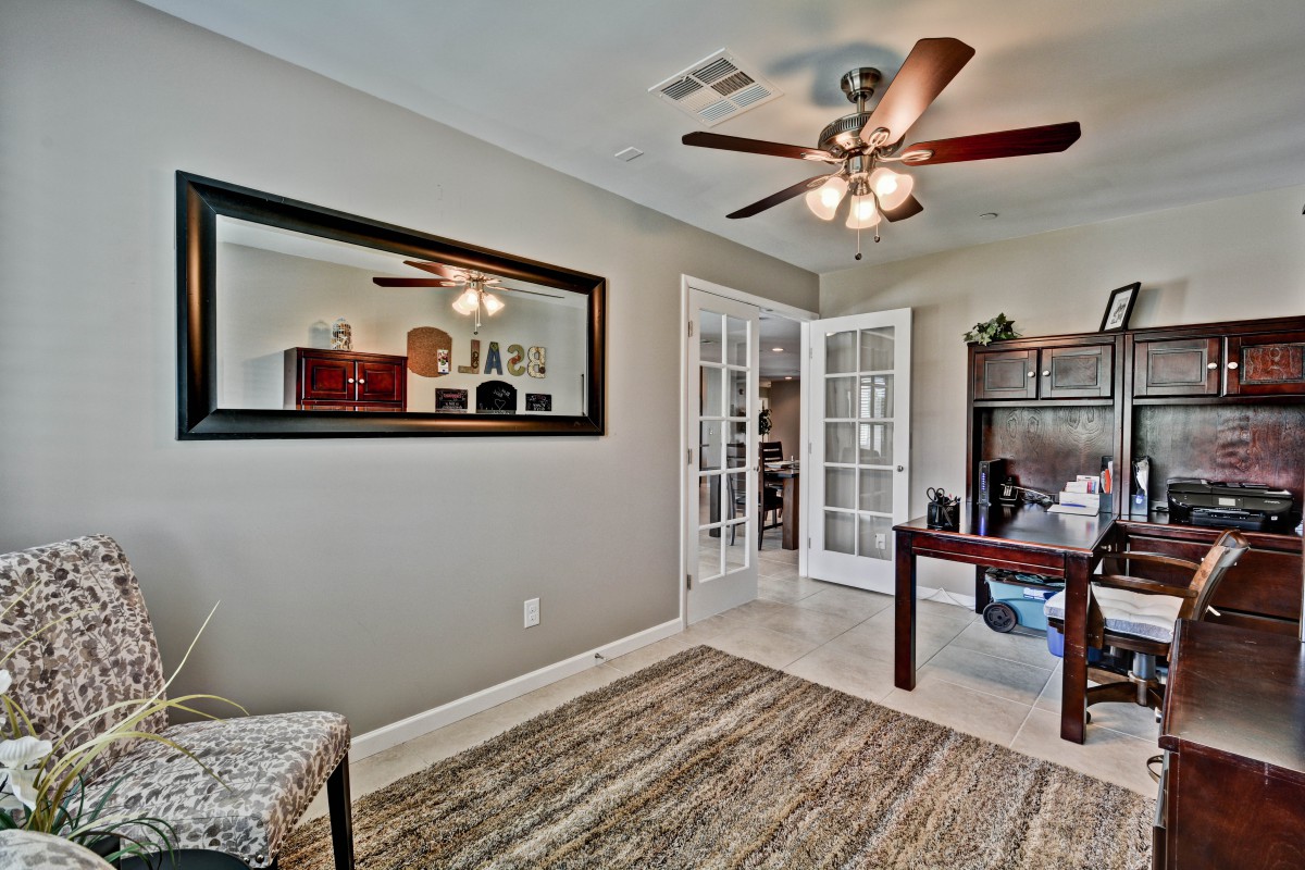 A cozy home office with a ceiling fan, French doors, and a stylish desk.