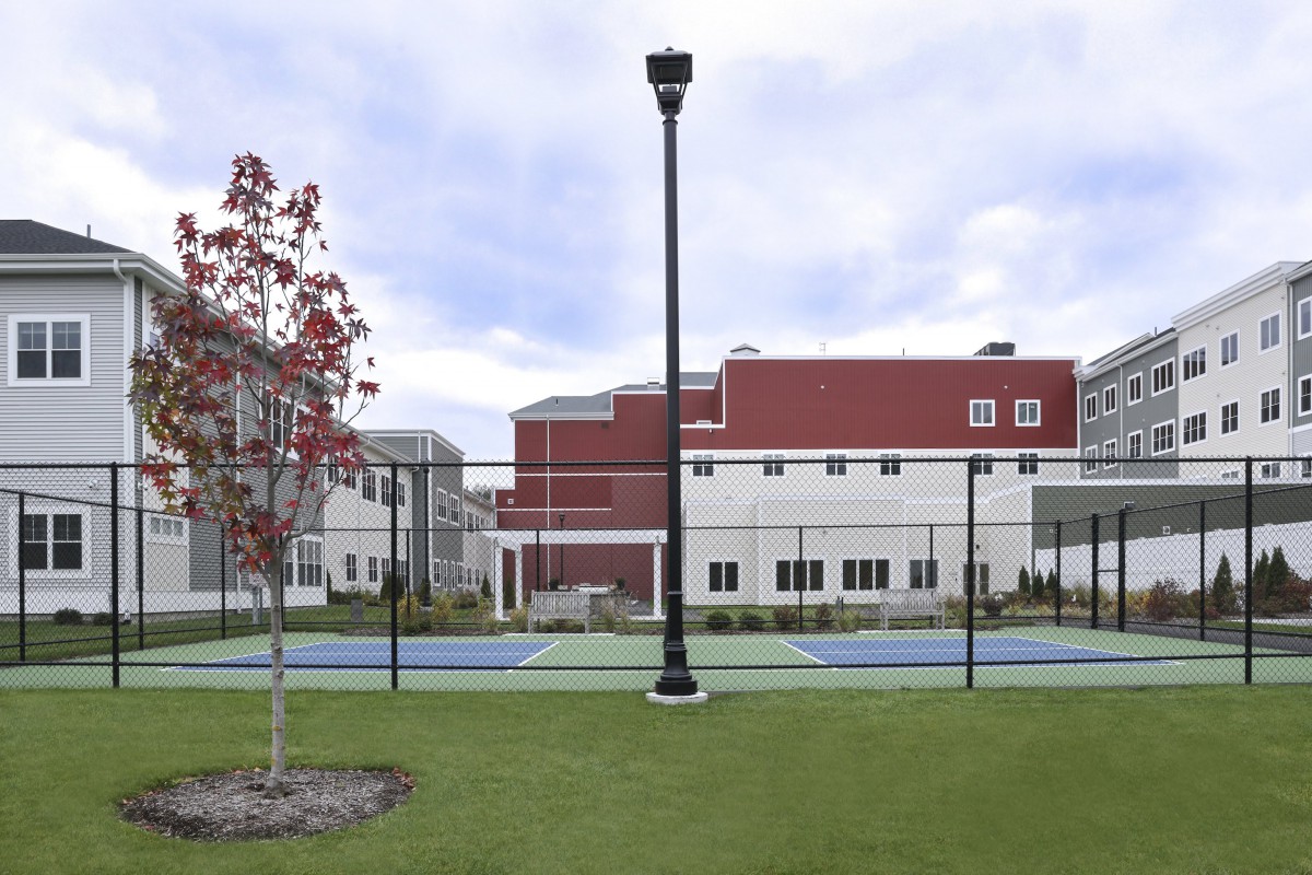 A tennis court enclosed by a fence with a lamp post nearby, adjacent to a building.