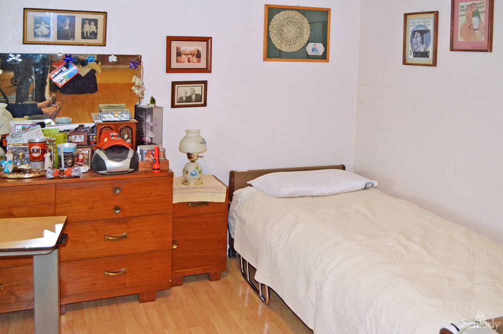 A vintage-style bedroom with a single bed and wooden dresser adorned with decorative items and wall art.