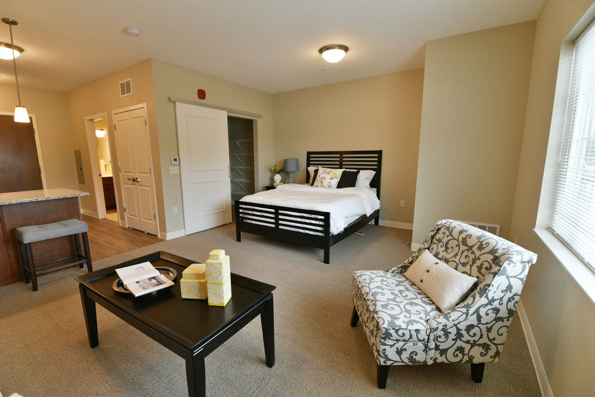 A cozy, well-decorated bedroom featuring a bed, patterned chair, and small table with candles.