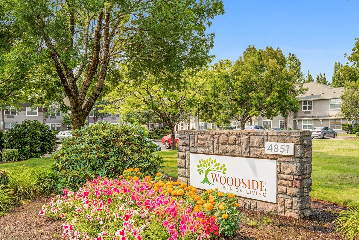 A landscaped entrance with a sign surrounded by vibrant flowers and lush trees.