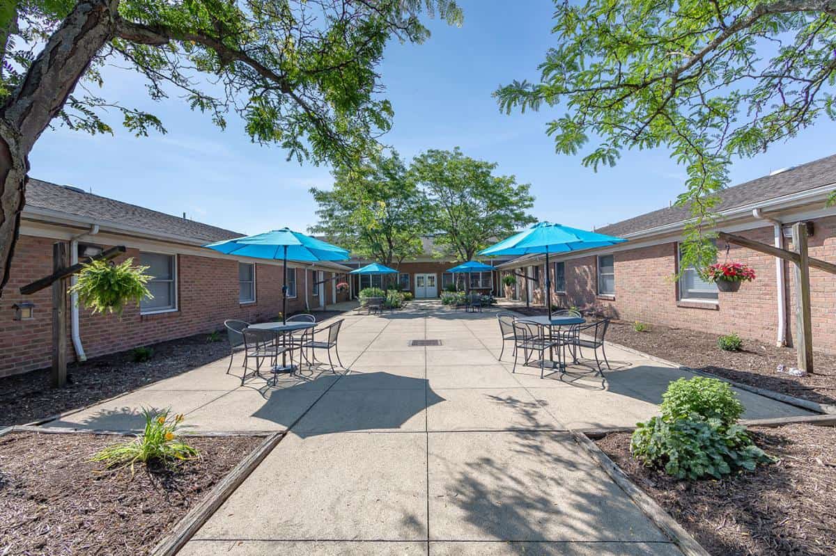 A sunny courtyard with tables, chairs, and umbrellas surrounded by brick buildings.