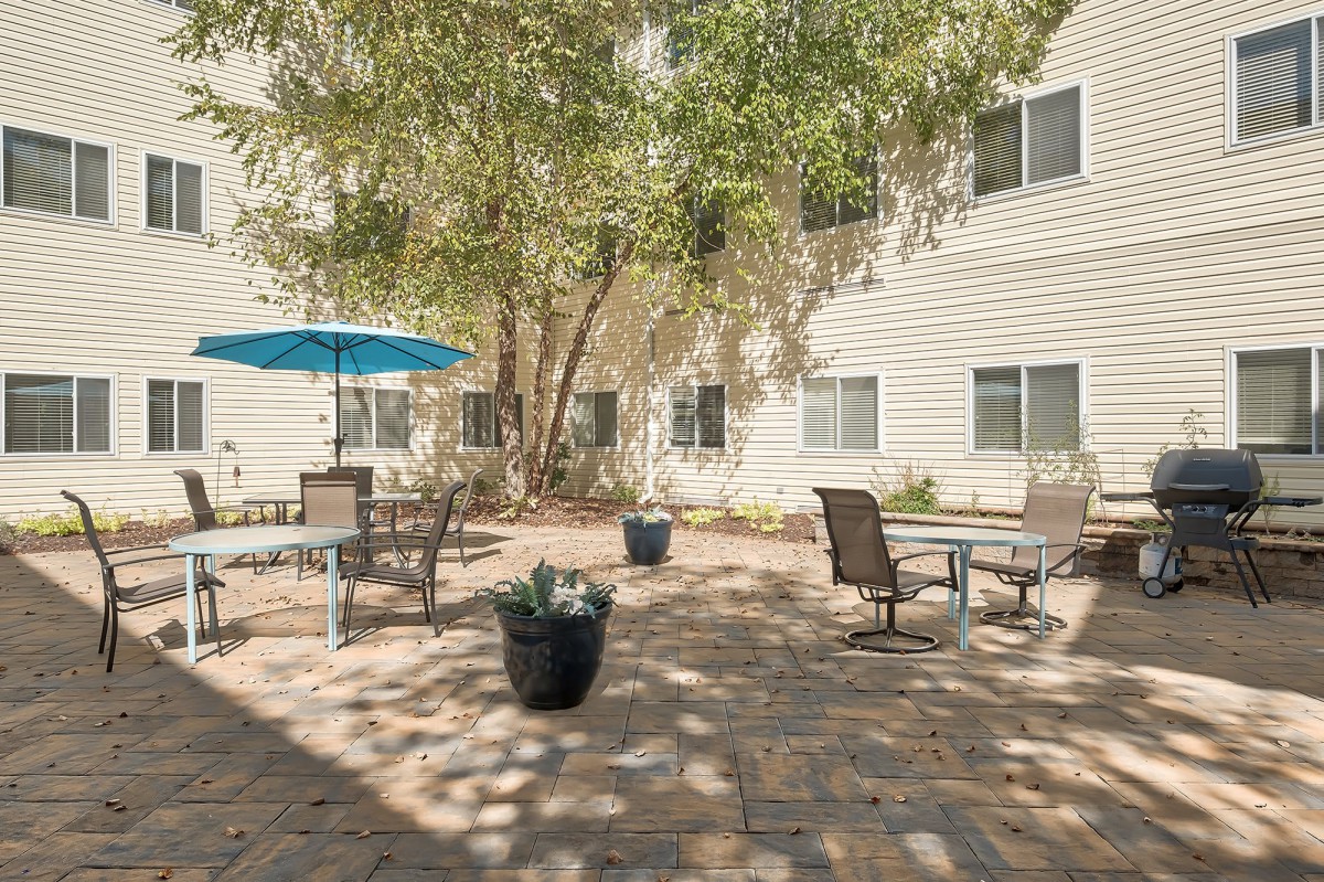 A tranquil courtyard with outdoor seating, shaded by trees and an umbrella.