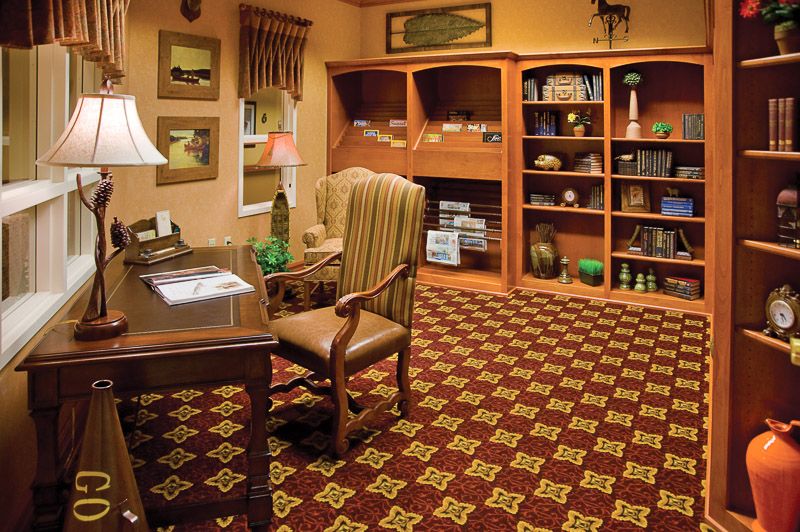 A cozy office space with a wooden desk, comfortable chair, and bookshelves filled with various items.