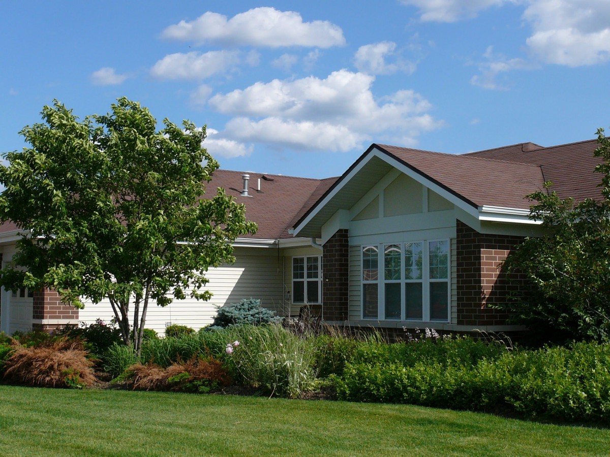 A suburban house with a well-maintained front yard and garden under a blue sky with scattered clouds.