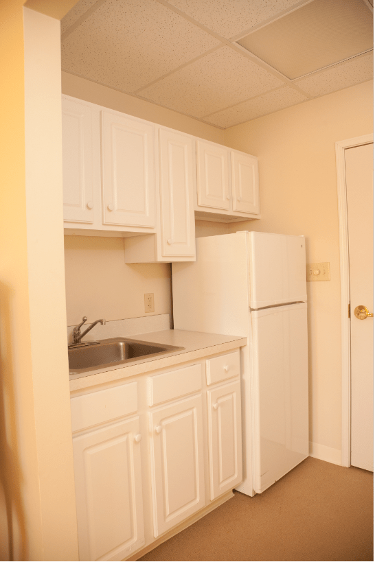 A compact apartment kitchen with white cabinets and a refrigerator.