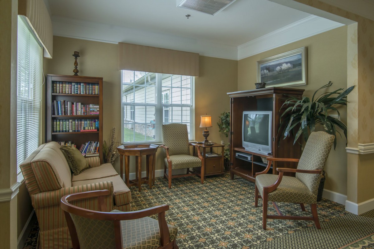 A cozy living room with comfortable seating, a TV, bookshelf, and a large window providing natural light.