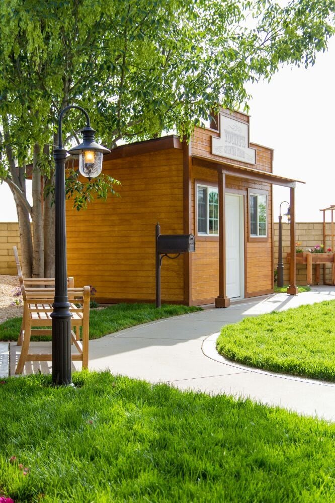 A charming wooden garden shed with a surrounding pathway and a lamp post, nestled in a well-maintained outdoor area.