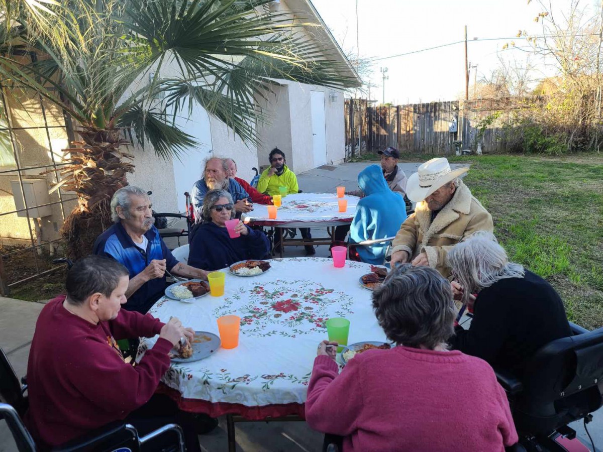 A group of people enjoying an outdoor gathering around a table in a garden setting.