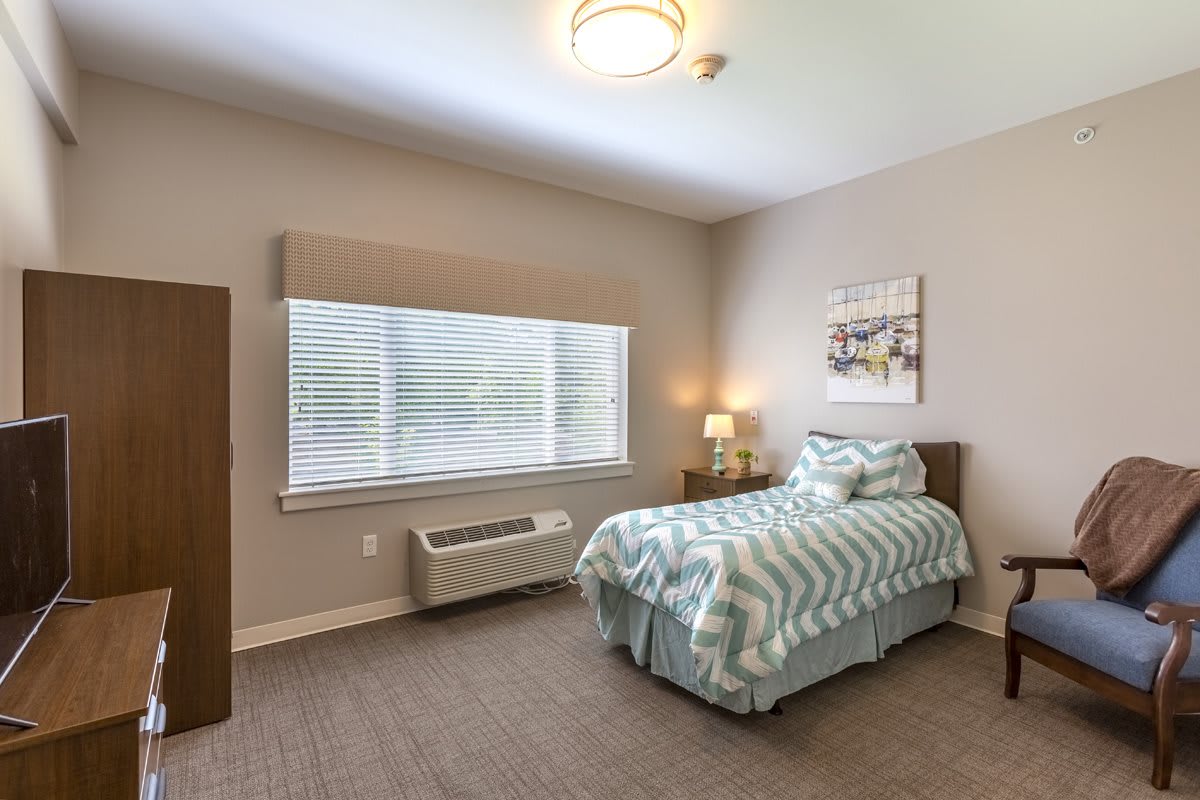 A minimalist bedroom with a single bed, bedside lamp, and a large window covered by curtains.