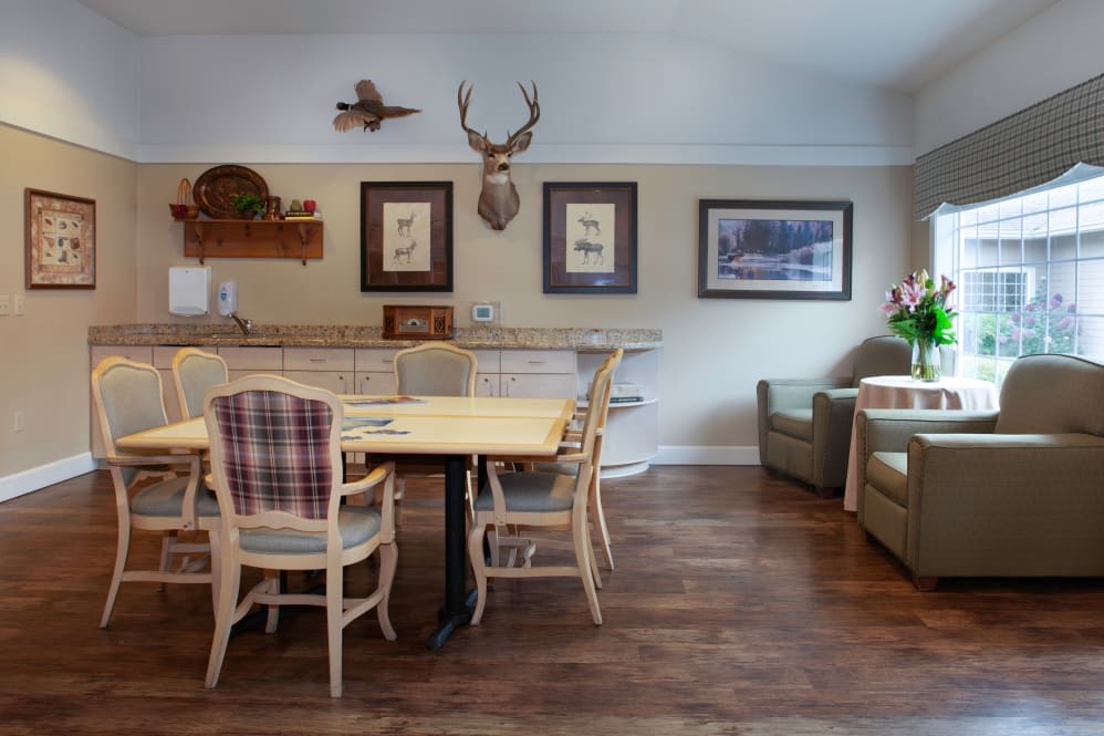 A cozy dining area with wooden flooring, featuring a table and chairs, decorative art on the walls, and a deer head mount.