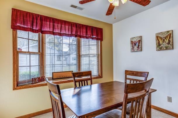 A cozy dining room with a wooden table and chairs near a large window adorned with red curtains.