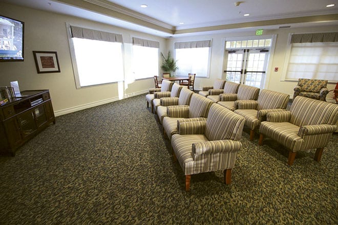 An empty waiting room with rows of cushioned chairs and large windows.