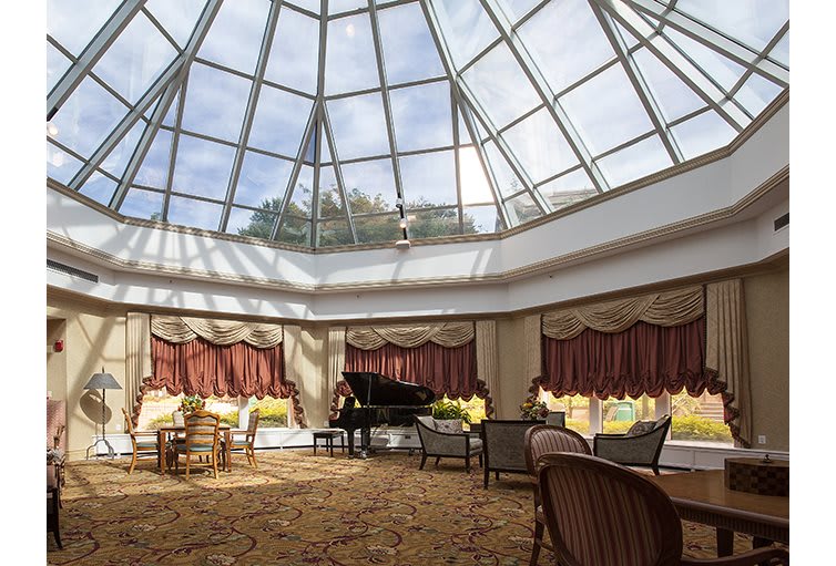 A spacious lounge area with a grand piano under a glass atrium, featuring elegant furniture and ample natural light.