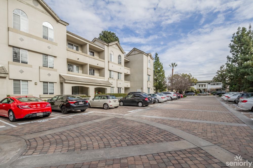 A view of an apartment complex with a parking lot filled with cars under a cloudy sky.