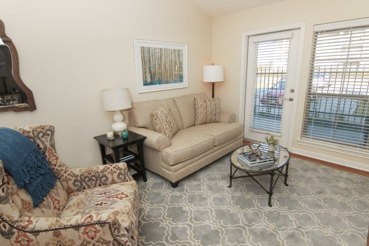 A cozy living room with a sofa, armchair, lamps, and a coffee table, featuring neutral tones and a geometric rug.