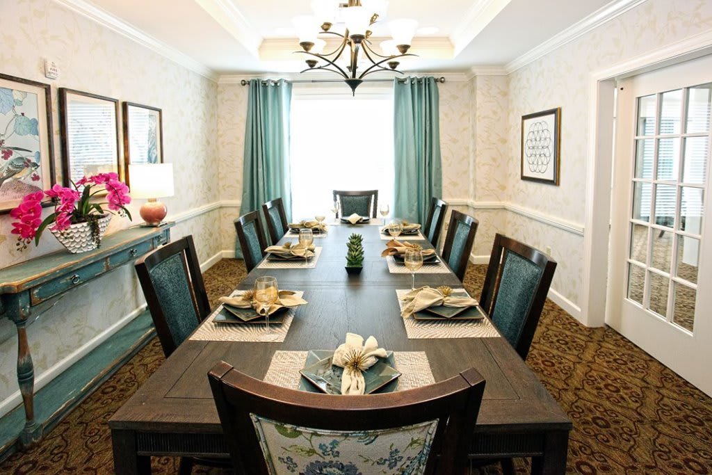 A well-decorated dining room with a long table set for a meal, featuring stylish chairs and a chandelier.