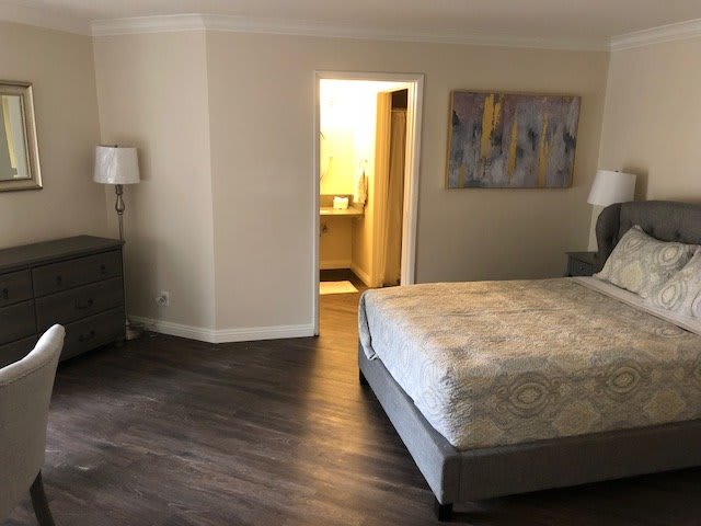 A modern bedroom with a neatly made bed, bedside lamp, and abstract painting.