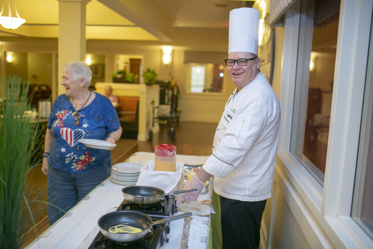 A chef in a white uniform and tall hat preparing food in a kitchen setting.
