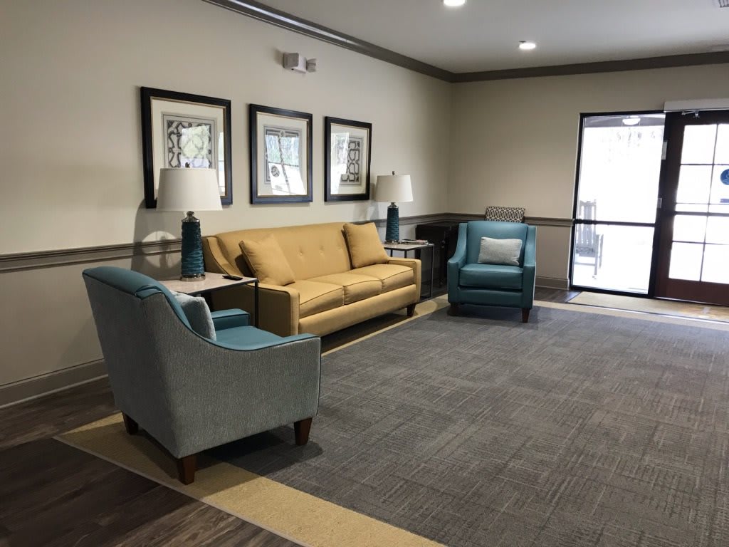 A cozy living room with beige and blue furniture, including a sofa and armchairs, complemented by lamps and framed artwork on the walls.