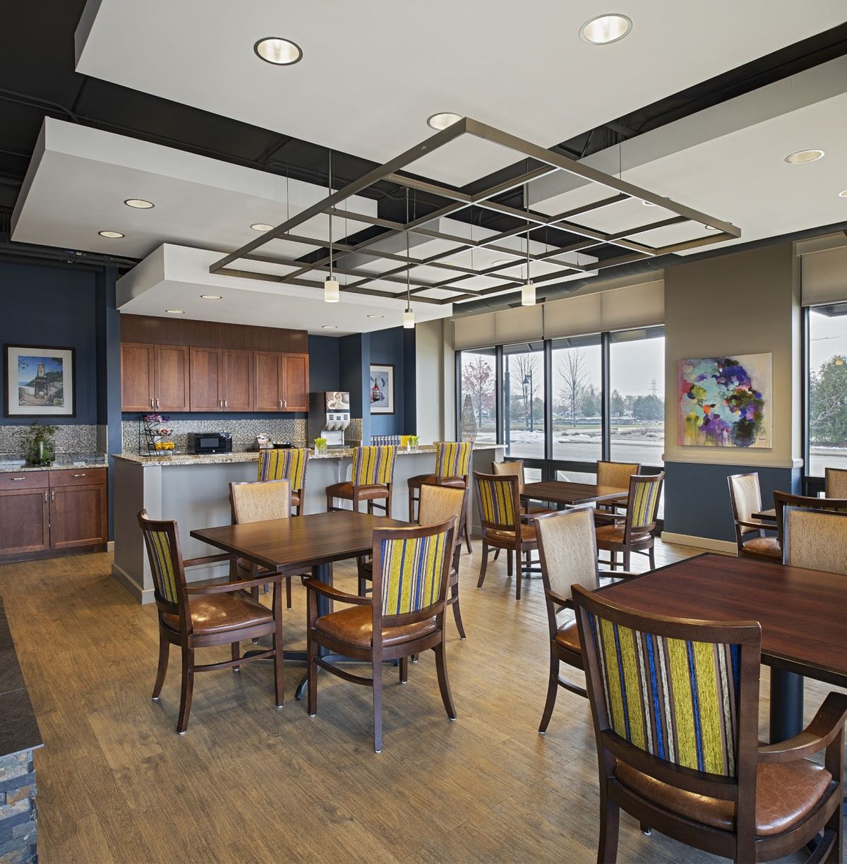 Modern dining area with kitchen, featuring tables, chairs, and large windows.