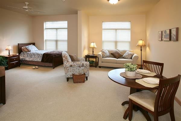 A cozy living space with a bedroom area, featuring a sofa, chairs, and a dining table.