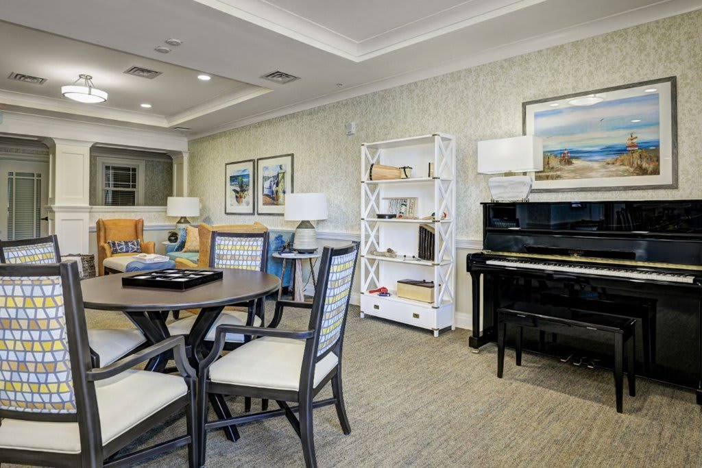 A cozy living room featuring a piano, round table with chairs, and a bookshelf adorned with decor.