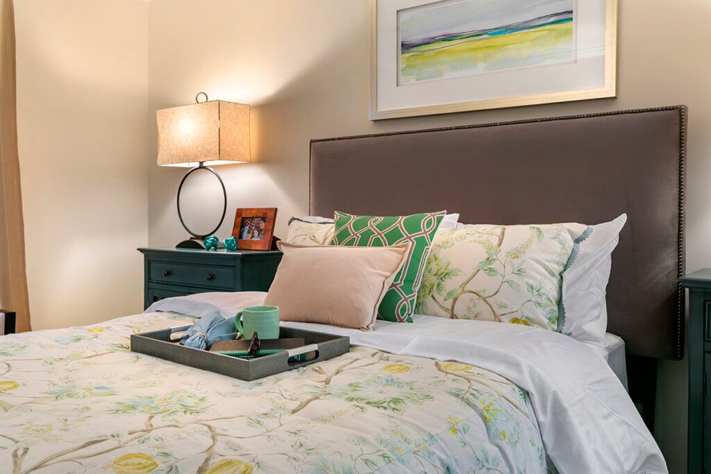 A cozy bedroom with stylish decor, featuring a neatly made bed, multiple pillows, and a bedside table with a lamp and decorations.