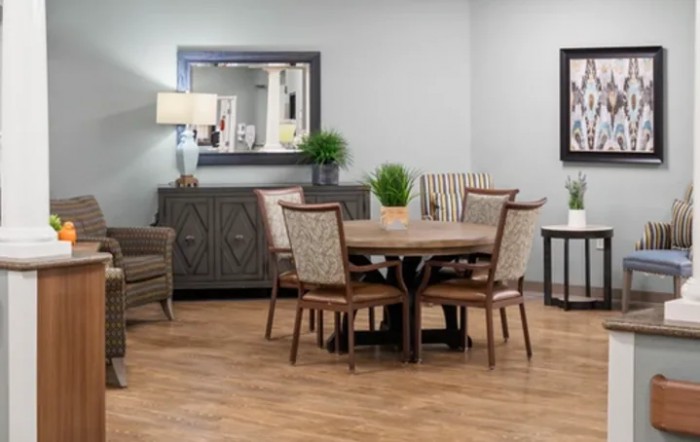 A cozy dining room featuring a round table with chairs, a sideboard with decorative plants, and a mirror on the wall.