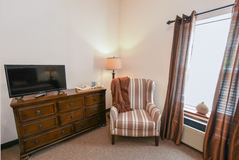 A cozy living room corner with a striped armchair, a lamp, and a dresser with a television.