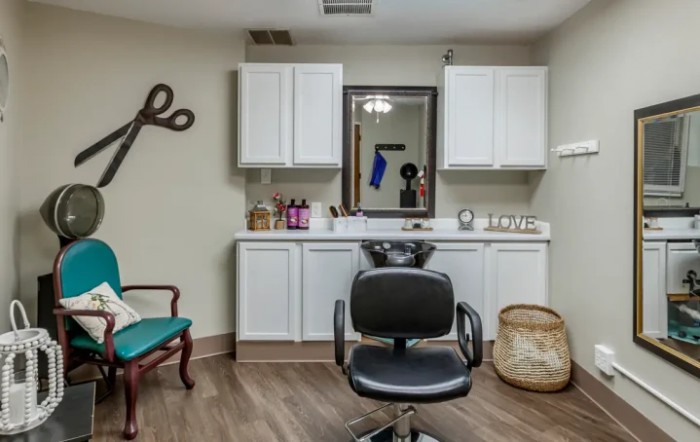A hair salon interior featuring a styling chair in front of a mirror and cabinets, with decorative scissors on the wall.