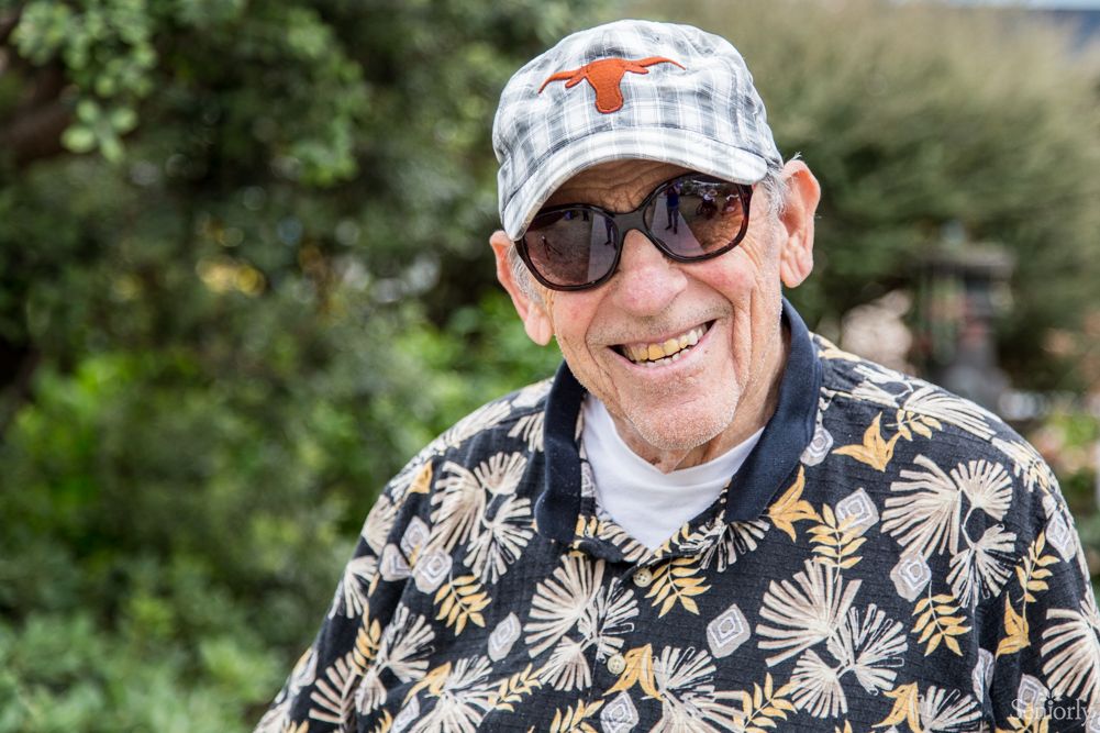 A smiling elderly man wearing sunglasses and a hat, enjoying time outdoors.