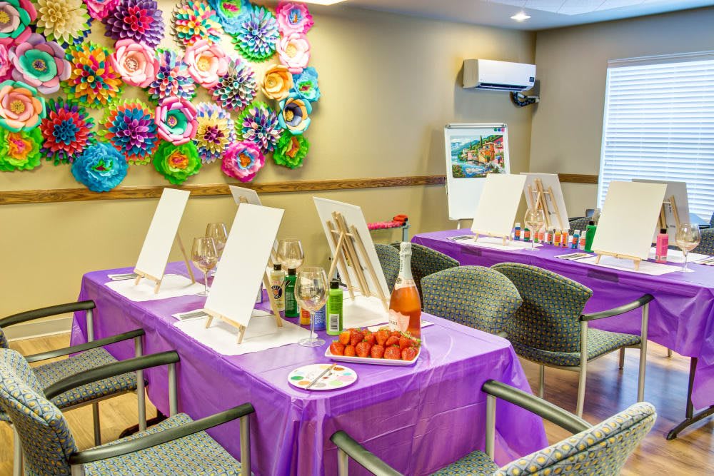 A colorful art workshop setup with canvases and painting supplies on purple-covered tables.