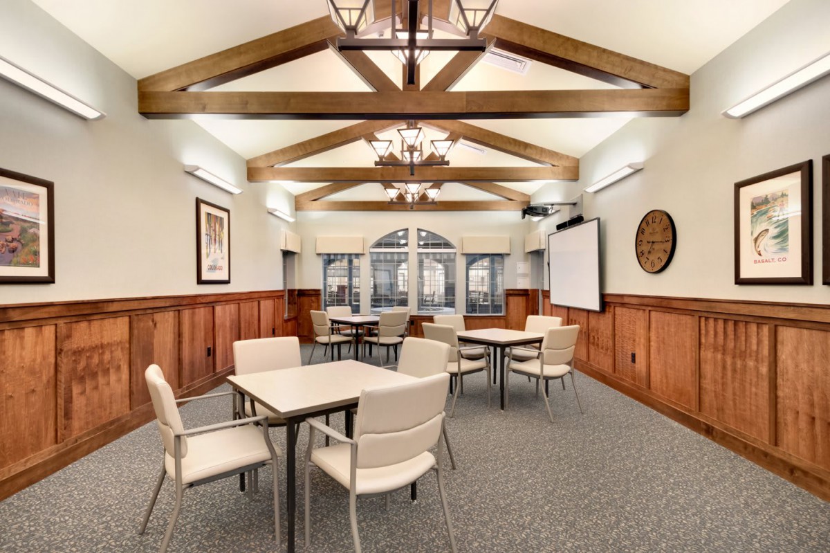 A stylish conference room with wooden beams and chandeliers, featuring tables and chairs arranged for a meeting.