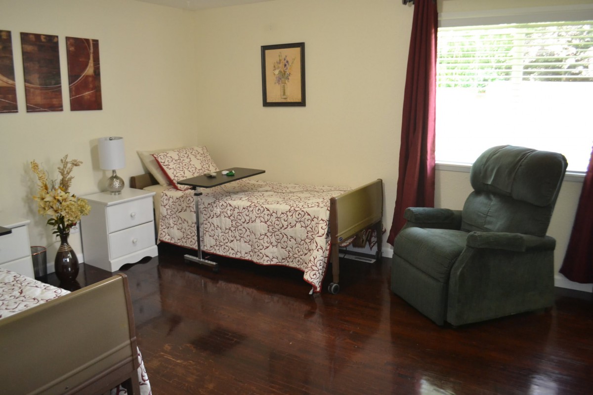 A cozy bedroom with a hospital bed, recliner chair, and wooden flooring.