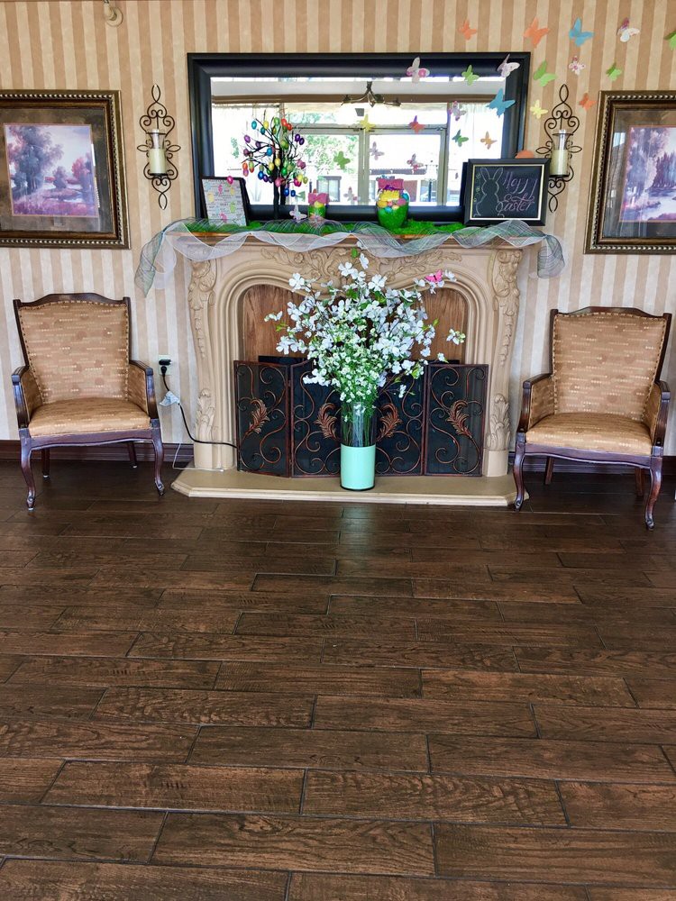 A cozy living room with a decorated fireplace, flanked by two upholstered chairs and a vase of flowers on a wooden floor.