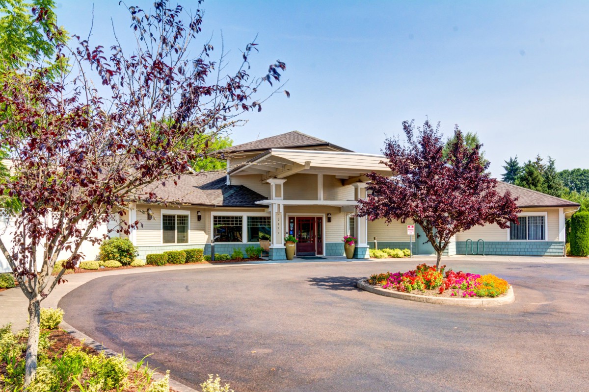 A well-maintained building surrounded by trees and flowers, with a circular driveway leading to the entrance.
