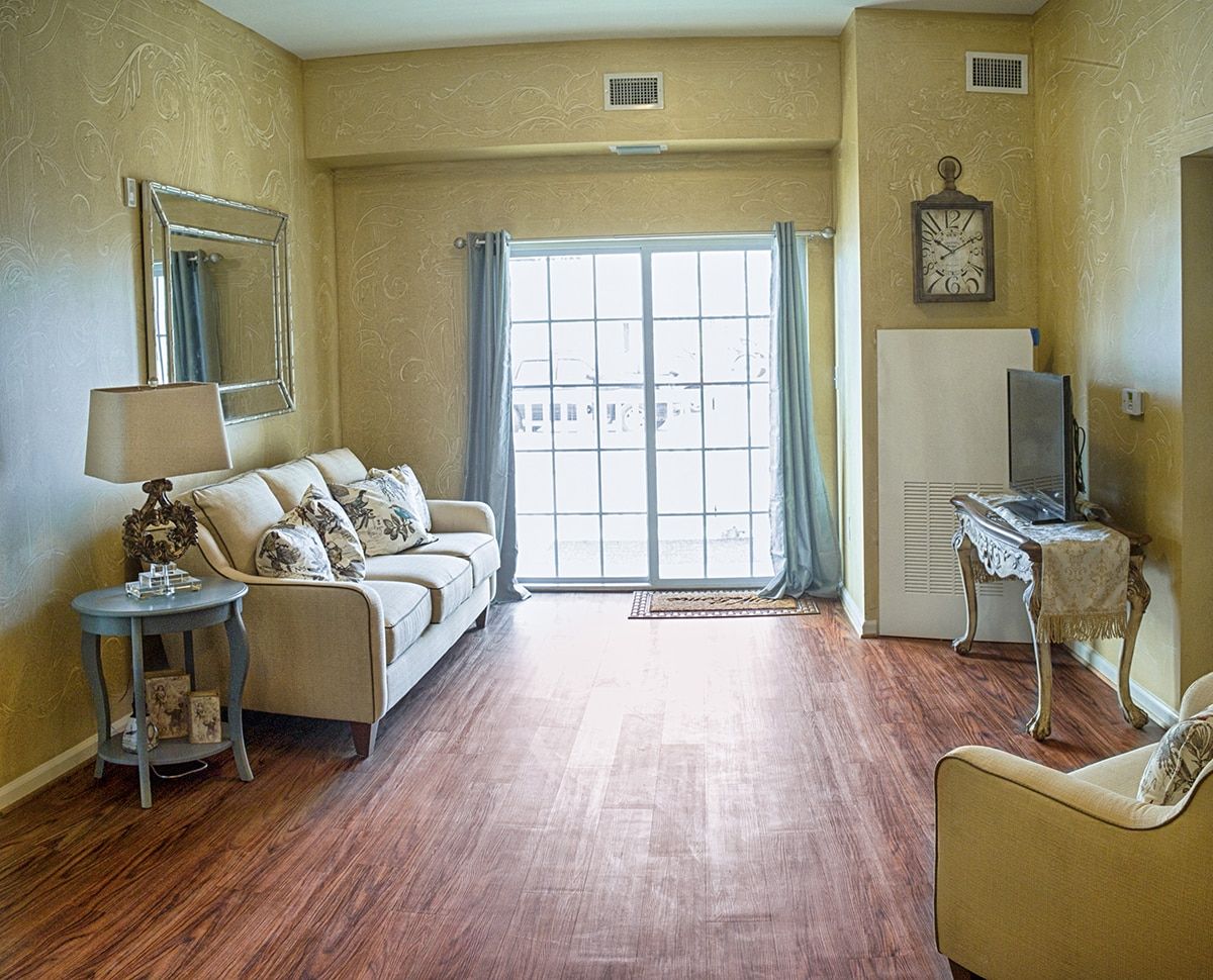 A cozy living room with a sofa, wooden flooring, and ample natural light streaming through large windows.