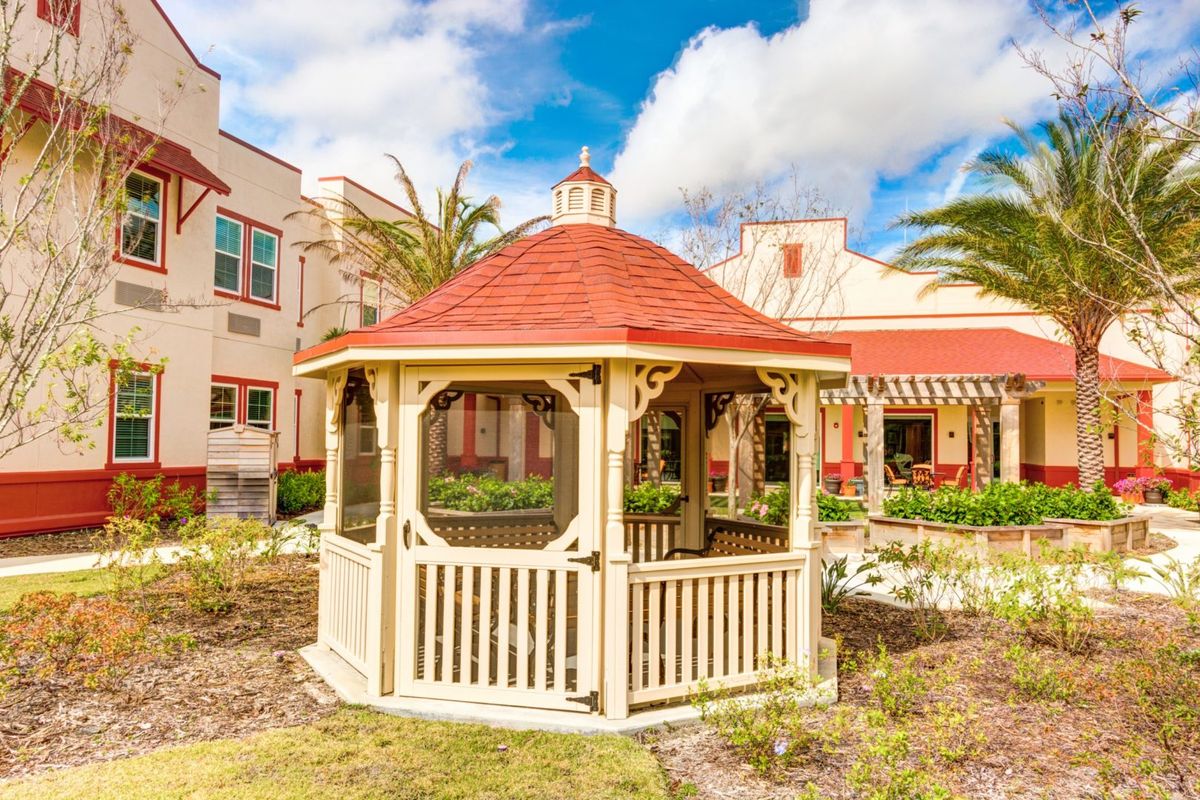 A charming gazebo situated in a landscaped garden on a sunny day, with buildings in the background.