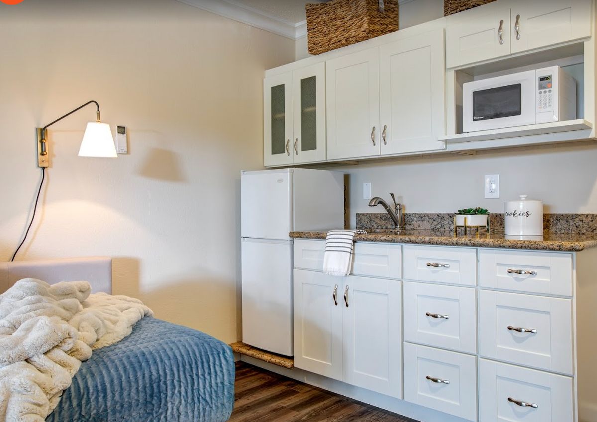 A cozy kitchenette with white cabinets, a small fridge, and a microwave.