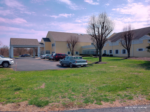 A view of a building complex with trees and parked cars on a grassy area under a cloudy sky.