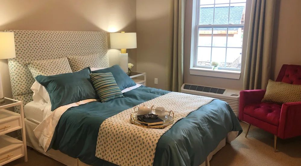 A cozy bedroom with a neatly made bed, decorative pillows, and a warm lamp by the window.