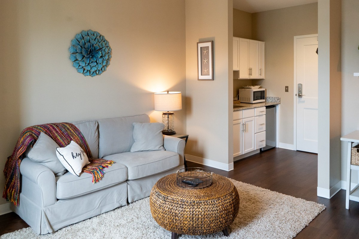 A cozy living room with a comfortable sofa, stylish decor, and a kitchen area in the background.