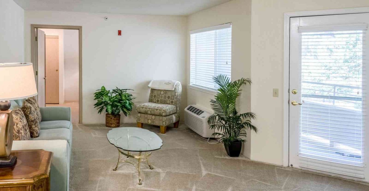A cozy corner with a chair, glass table, and indoor plants near a window.