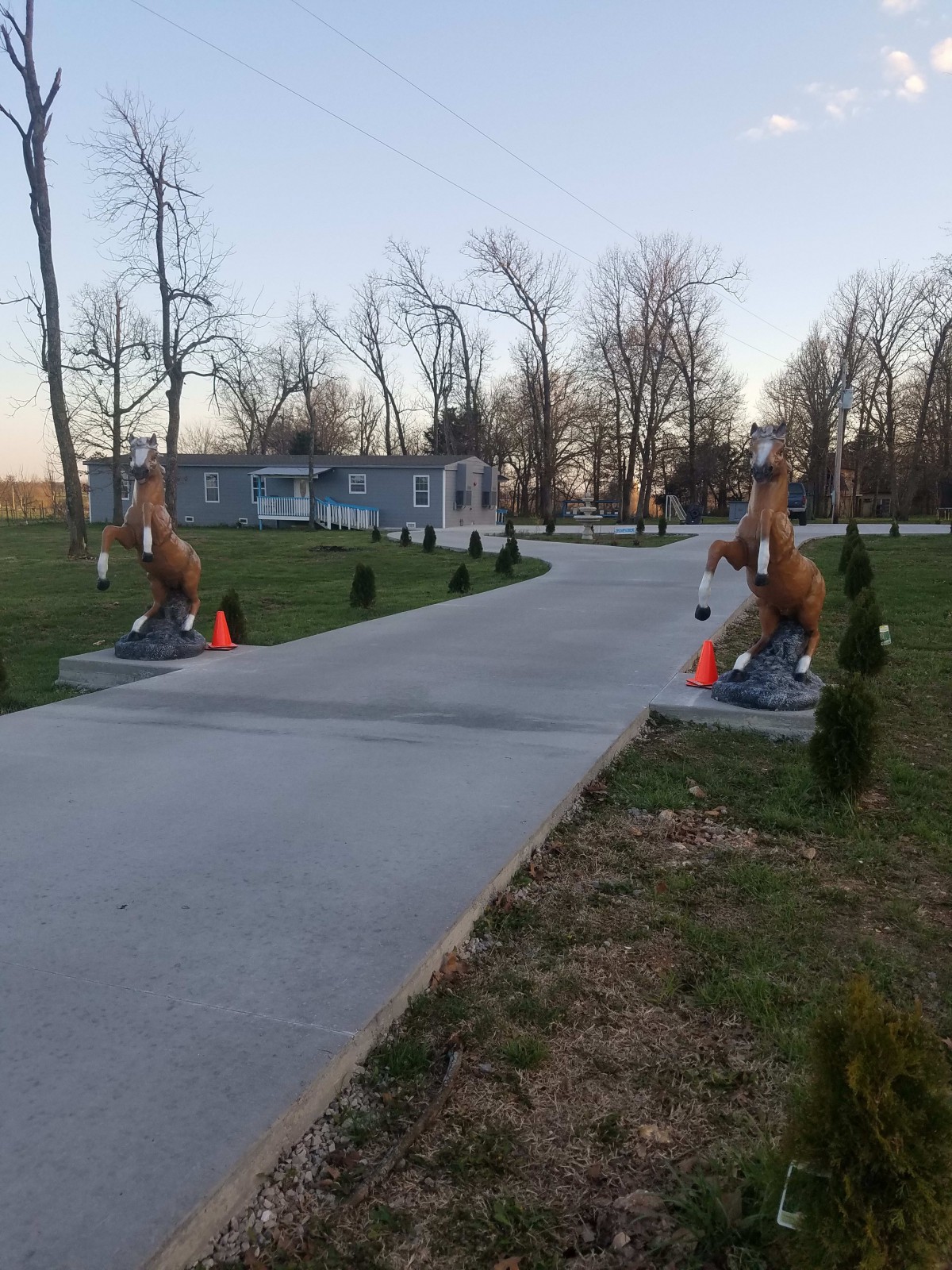 A concrete driveway lined with horse statues leads to a house surrounded by trees.