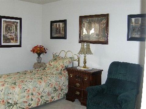 A cozy bedroom featuring a floral-patterned bed, a side table with a lamp, and an armchair.