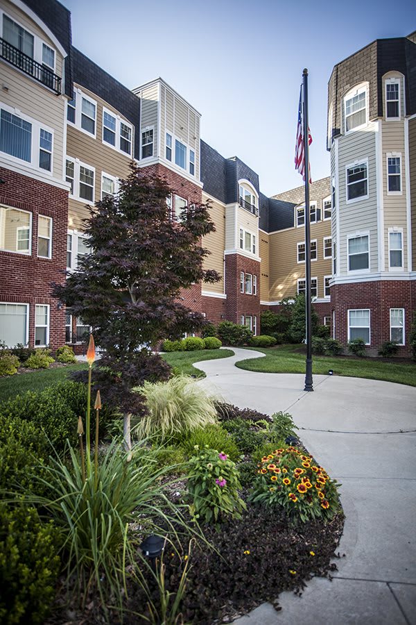 A view of an apartment complex with well-maintained landscaping and a flagpole along a curved pathway.