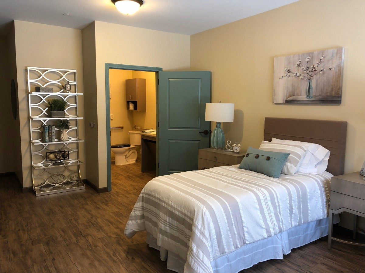 A cozy bedroom featuring a single bed, wooden floors, and a small dresser with a lamp.